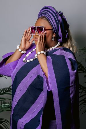 Fashion portrait with purple head wrap, oversized sunglasses, beaded jewelry and striped purple fabric.
