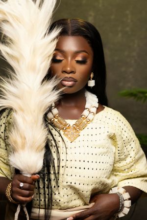 Elegant portrait with cream knit sweater, gold jewelry and dramatic white feather prop.