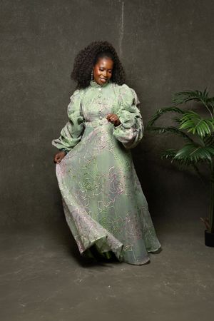 Joyful portrait in mint green brocade dress with puff sleeves against dark background.