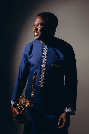 Dramatic portrait of saxophonist wearing navy African-inspired outfit with white embroidery.