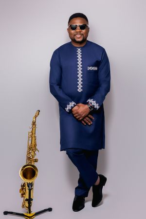 Stylish musician posing with saxophone in navy traditional dress and sunglasses.