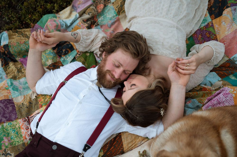 Couple relaxes on colorful picnic blanket surrounded by nature.