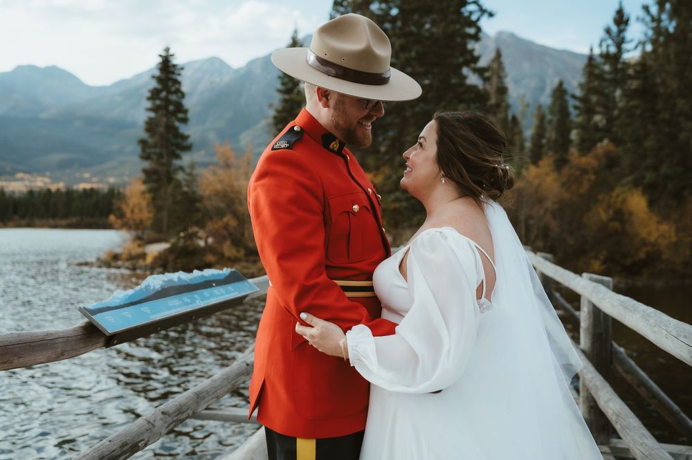 Wedding couple shares intimate moment on wooden dock with mountain lake backdrop.
