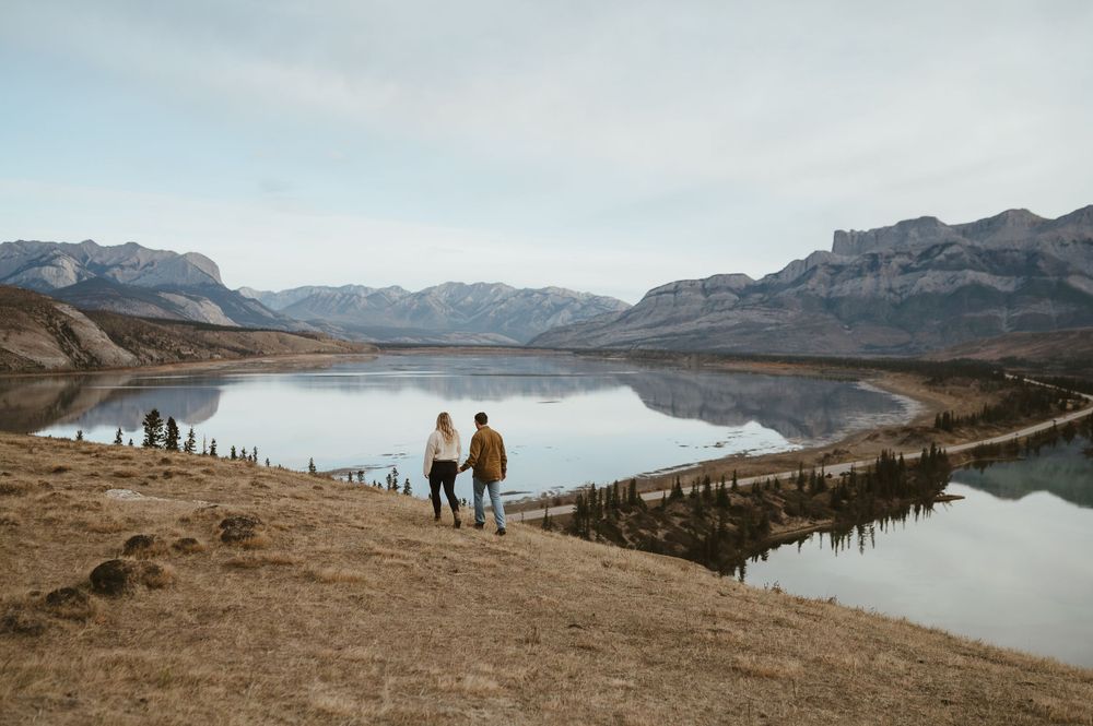 Two figures silhouetted against stunning mountain lake landscape at sunset.