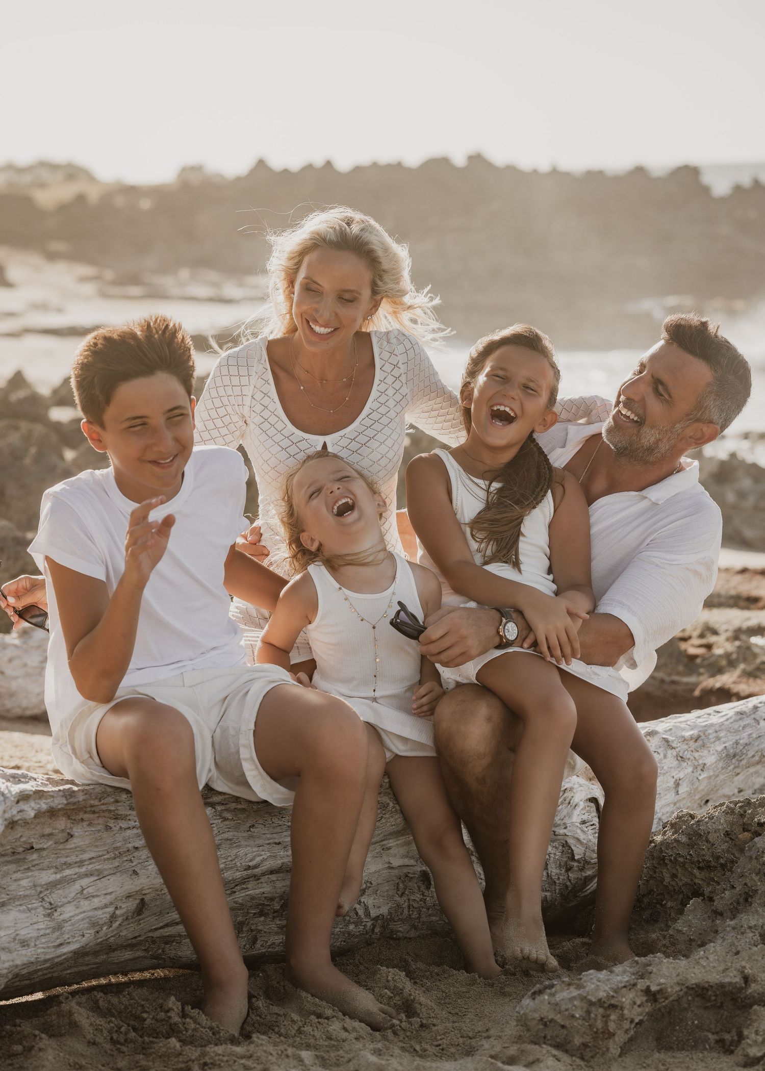 Group posing triumphantly on coastal rocks at beach during sunset.