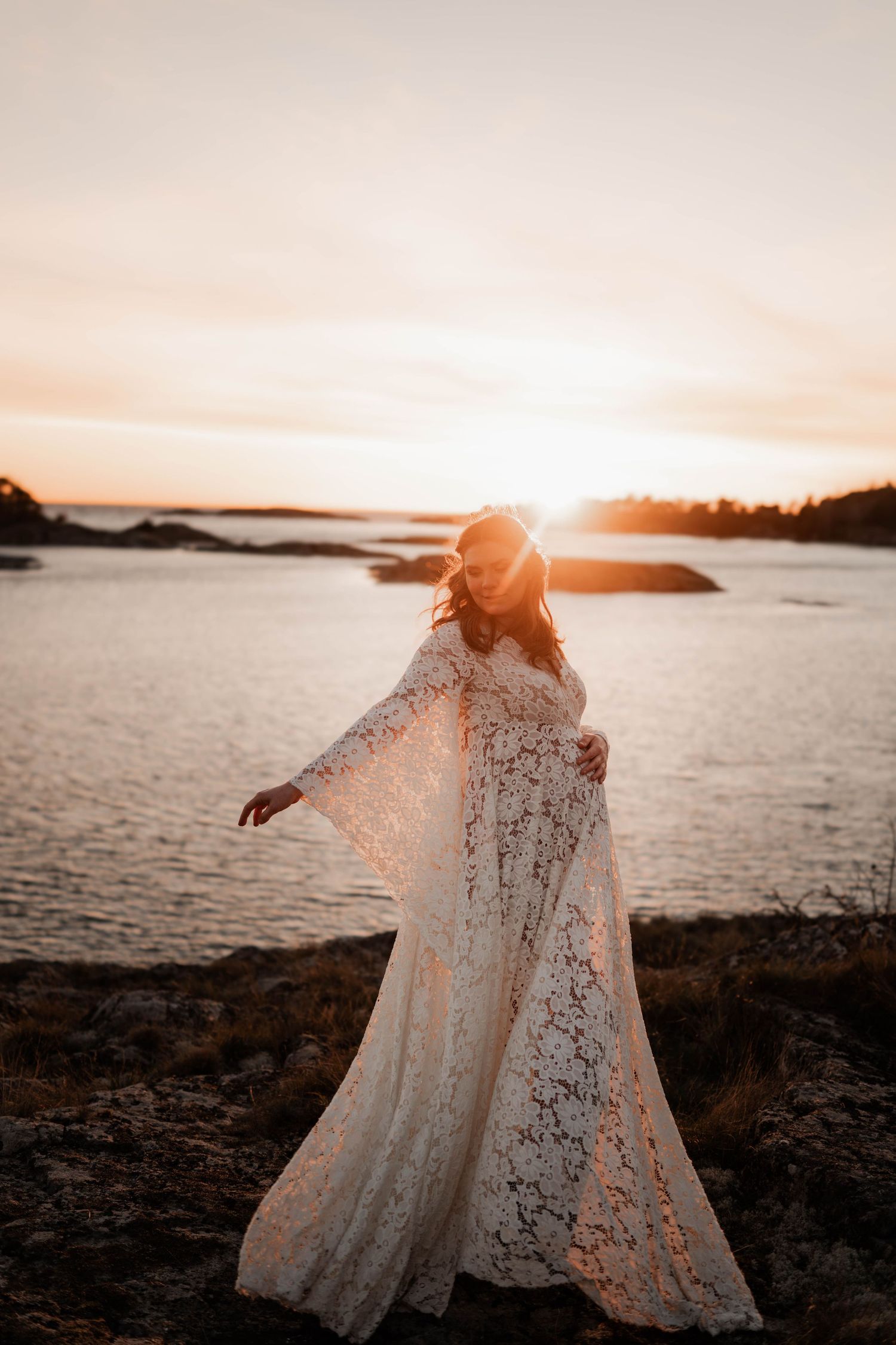 Gravid kvinna på klippor i solnedgång med vacker gravidklänning