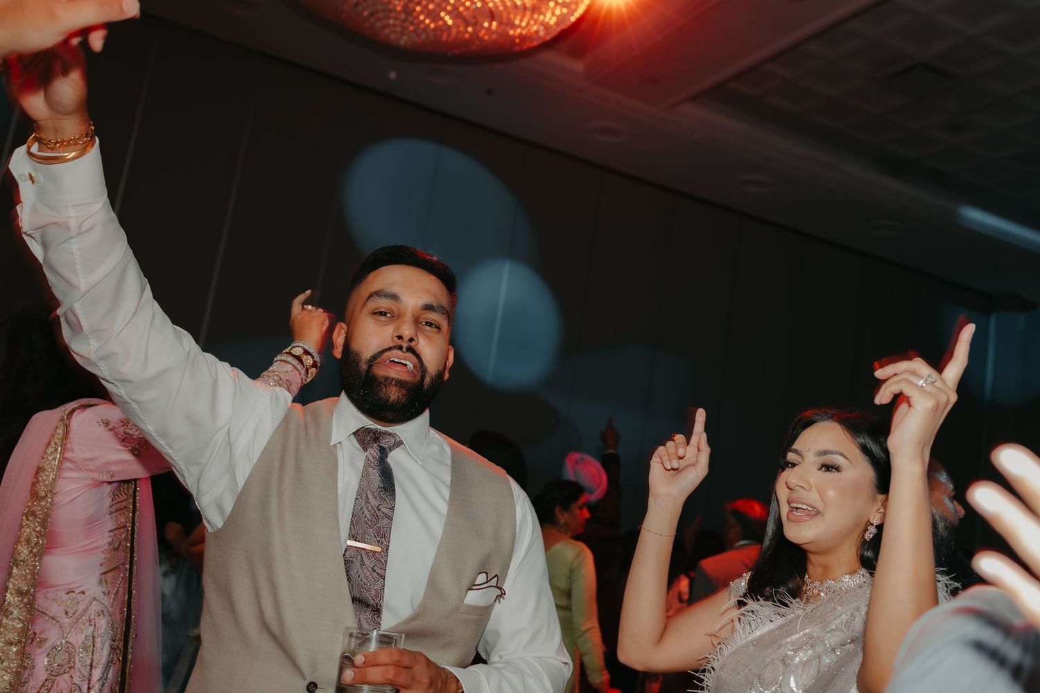 A couple dances joyfully together at a wedding reception celebration with raised hands.