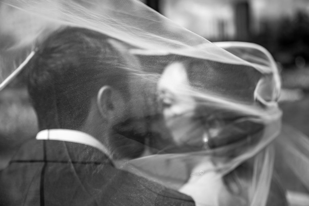Black and white wedding photo of bride and groom kissing under a flowing veil.