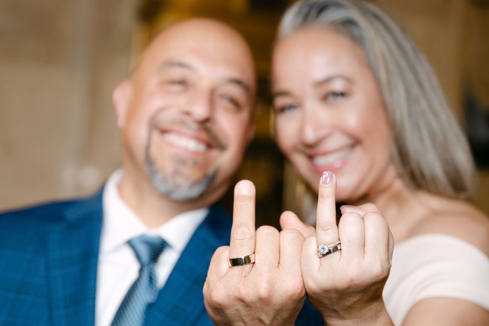 Smiling couple showing off wedding rings on their fingers in a joyful close-up celebration photo.