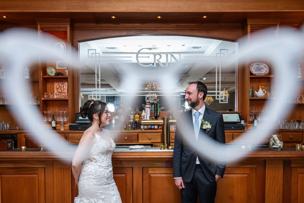 Bride and groom pose romantically inside a wooden bar framed by heart-shaped bokeh, with Grin sign behind them.