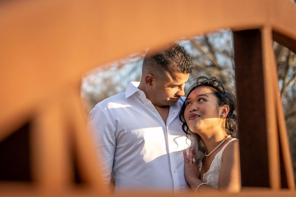 Romantic couple sharing an intimate moment, framed by rustic wooden structure in warm golden sunlight.