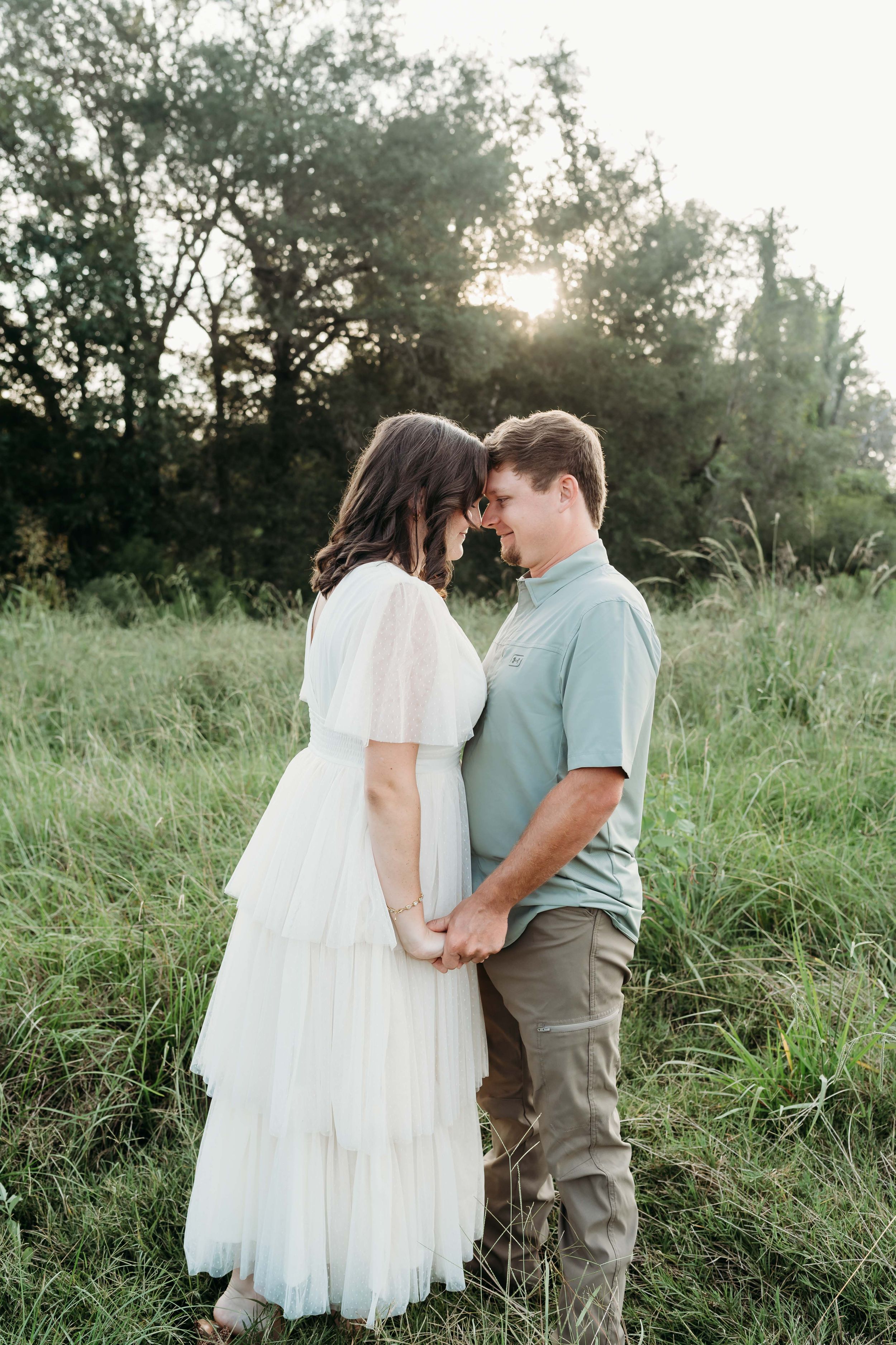 A couple shares an intimate moment while holding hands in a sunlit meadow.