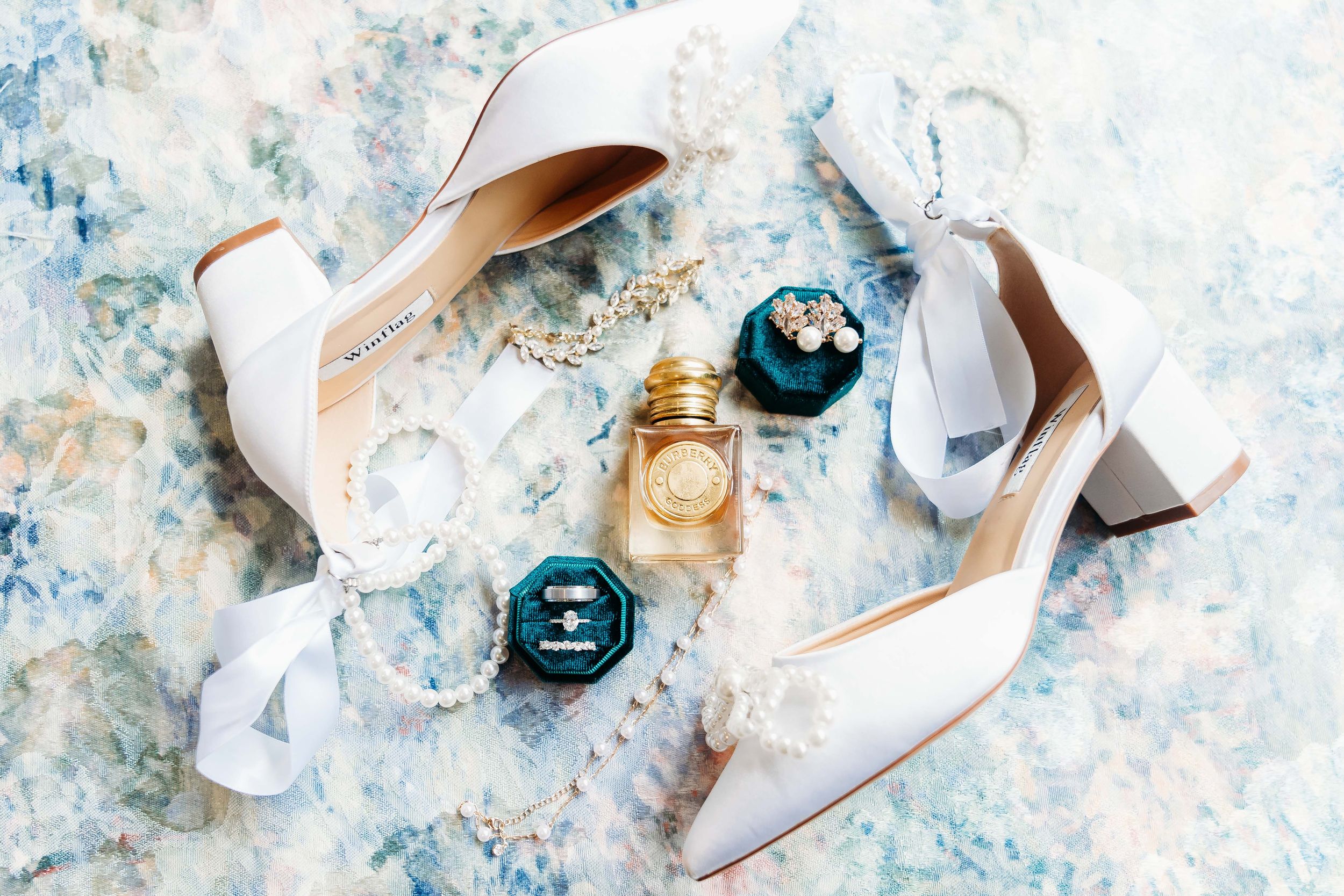 Elegant white wedding shoes, perfume bottles and blue ornaments arranged on marble.