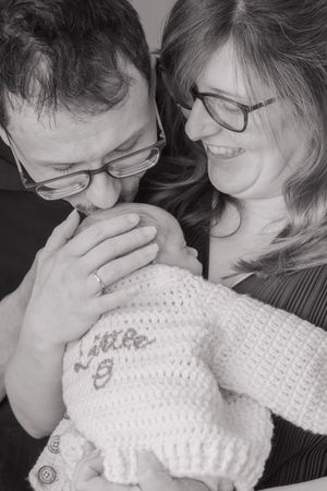 Black and white, young couple with newborn first baby, dad is giving baby a kiss on the head