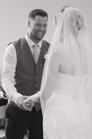 A black and white image of a bride and groom during their wedding ceremony. The groom has the biggest smile, whilst looking at his bride.