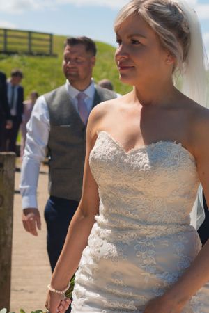 Bride and groom are leading their guests. The focus is on the bride gazing into the distance, with the groom out of focus just behind.