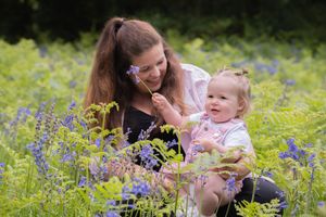 Mum and little girl in field of flowers, bluebells, they are playing and laughing with each other.
