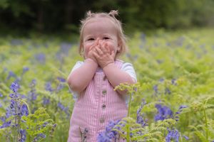 Little girl in field of flowers, bluebells, holding her hands over her mouth and laughing