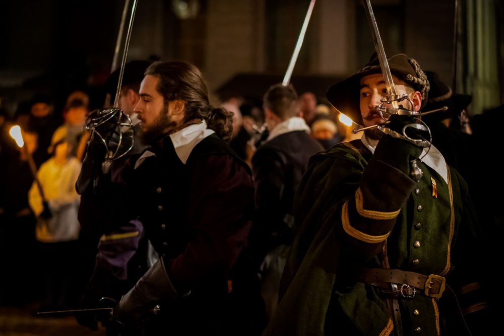 Costumed reenactors with muskets perform in front of nighttime crowd.