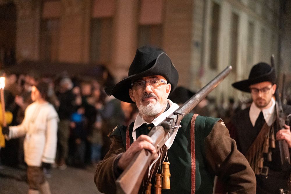 Colonial reenactor in traditional dress aims a vintage musket during an evening event.