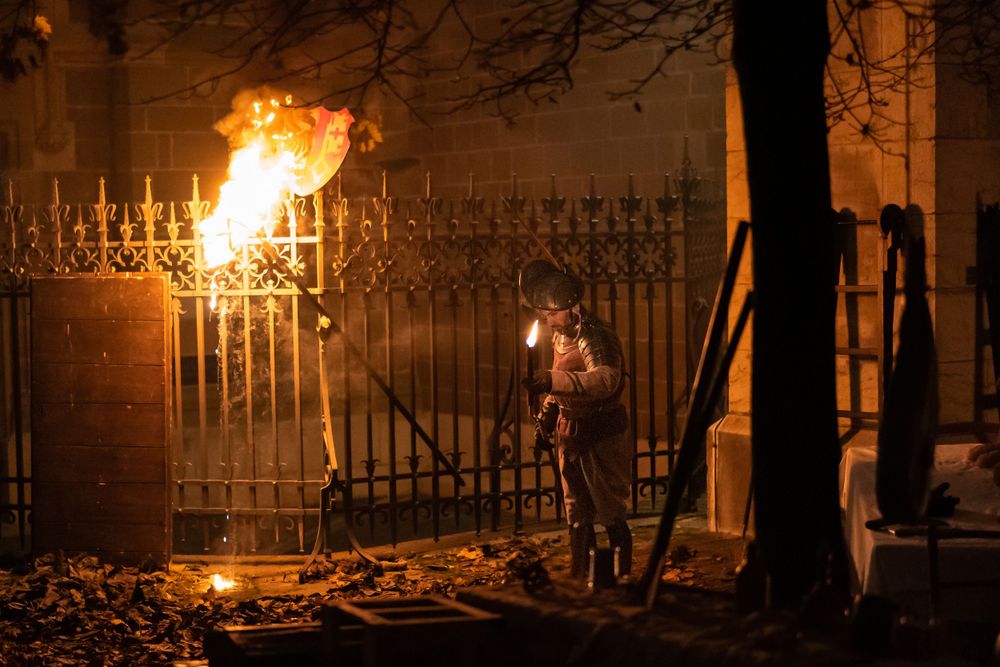 Flaming torch illuminates an ornate iron gate at night.