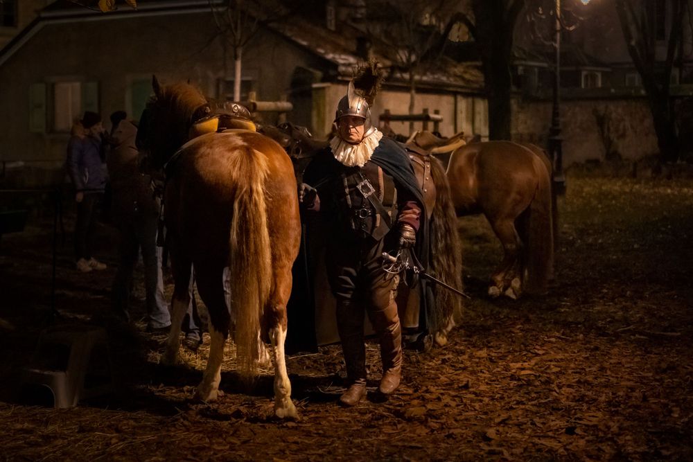 Horse and handler illuminated by warm lighting in a nighttime stable scene.