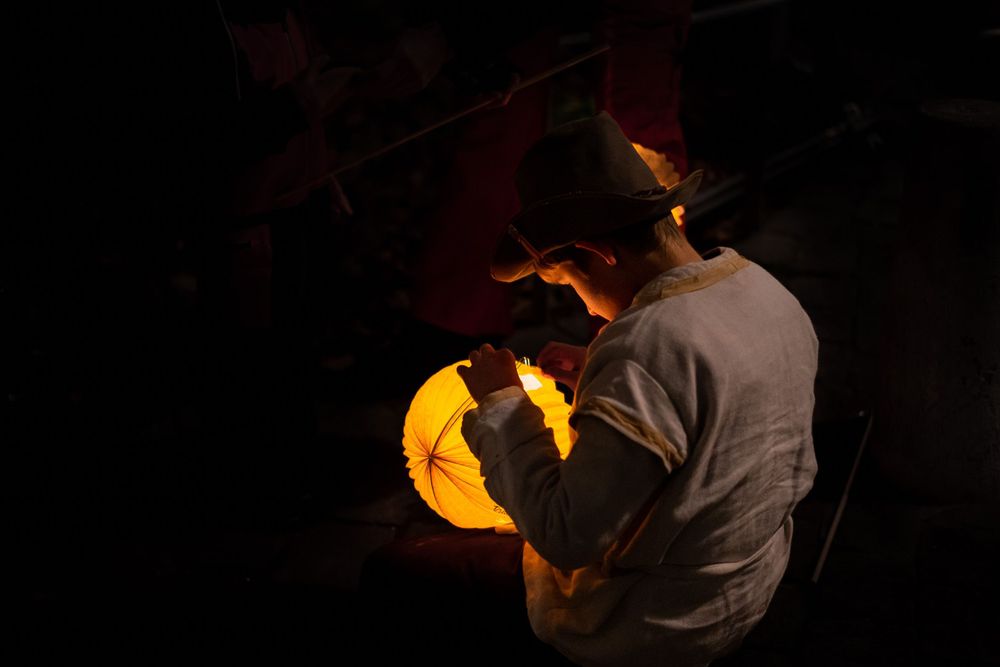 Silhouette holding a glowing orange lantern against a dark background.