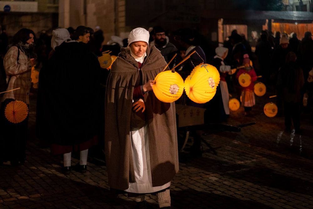 Person in traditional dress carrying glowing paper lanterns during a nighttime festival.
