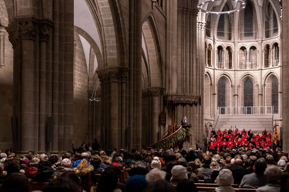 A large choir in red robes performs inside a grand cathedral with gothic architecture and arched ceilings.
