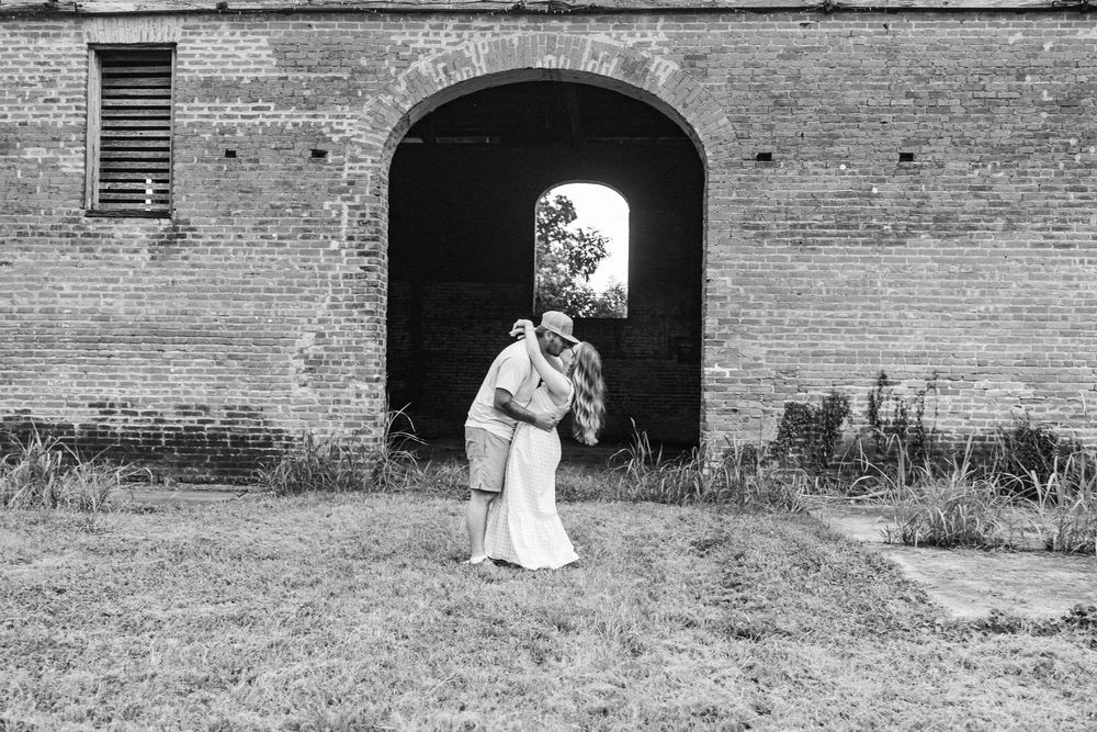 A romantic couple in wedding attire stands in front of an old brick wall with arched doorways during their photoshoot.