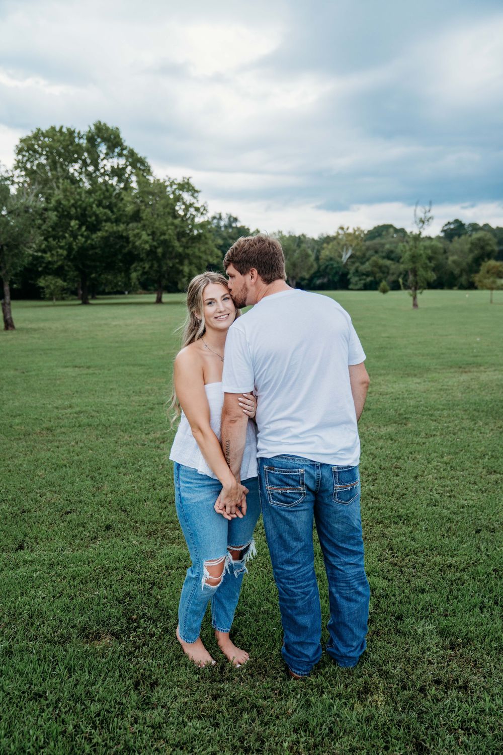 A family in matching denim outfits holds hands while standing together in a grassy field on a cloudy day.