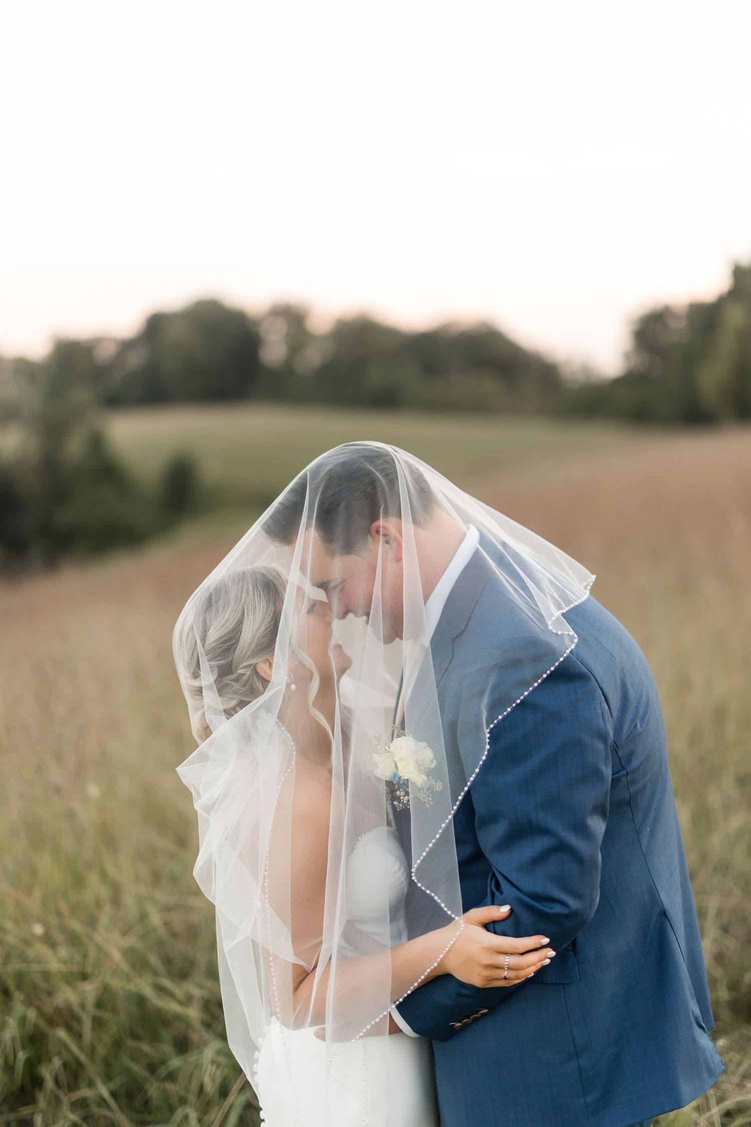 Romantic wedding photo of a couple in intimate embrace at sunset, bride in white and groom in brown suit with floral boutonniere.