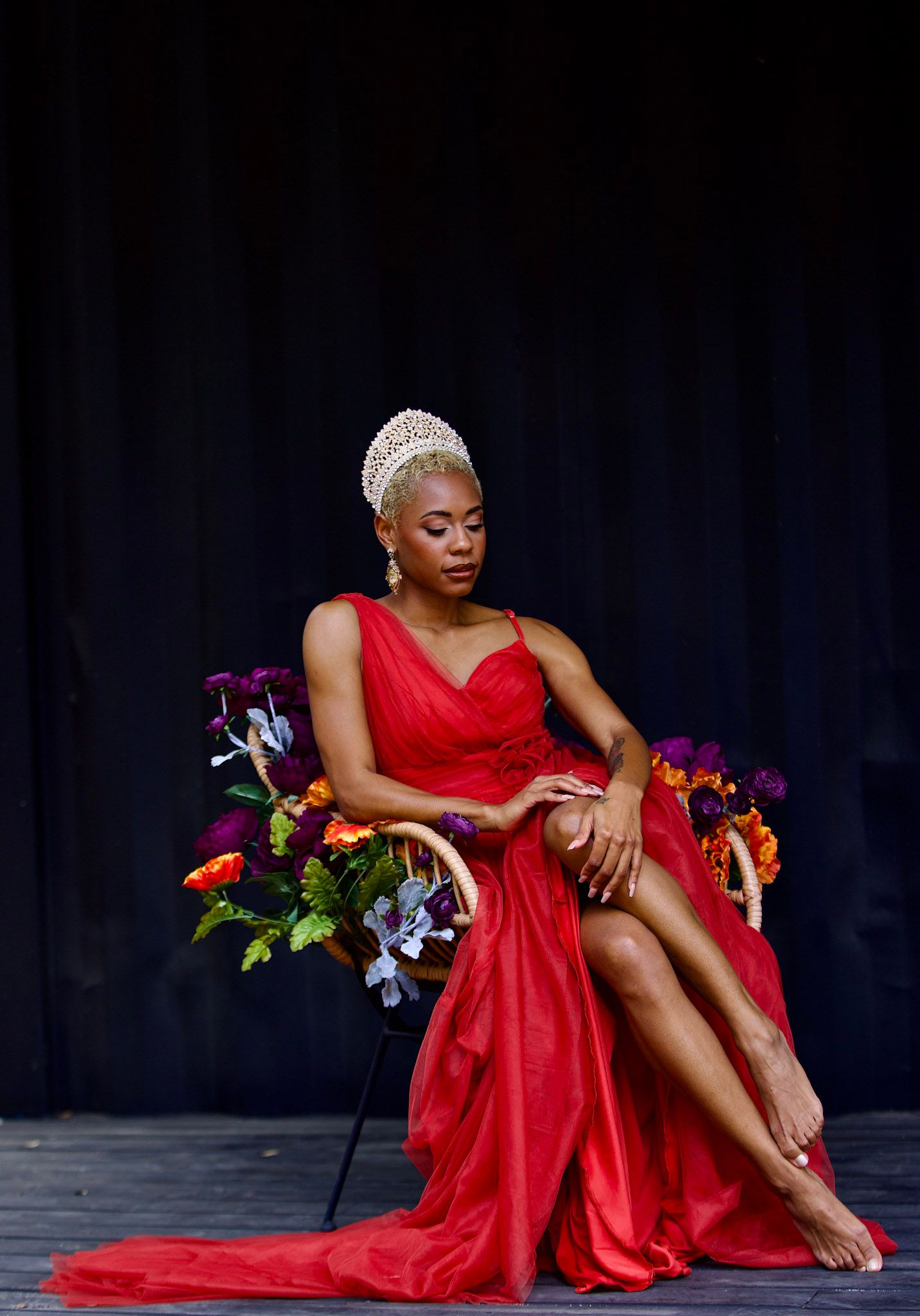 Woman in flowing red dress posing gracefully with colorful flowers on dark stage.