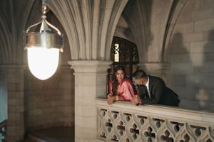 A couple leans on a gothic stone balcony under vintage pendant lighting.