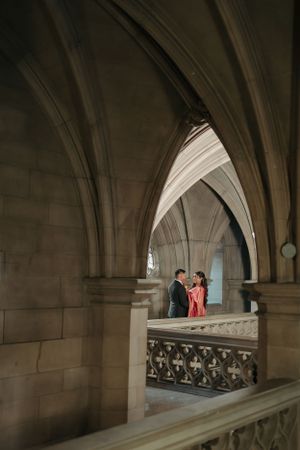 Elegant architectural shot of a couple framed by gothic stone arches and balustrades.