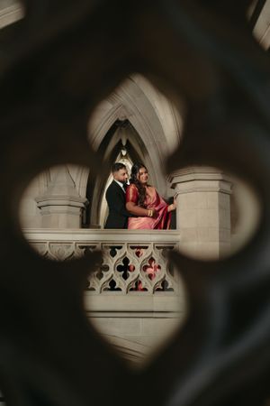 Artistic view through quatrefoil window frame of couple in gothic cathedral setting.
