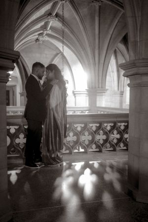 Black and white photo of couple in intimate moment under cathedral arches.