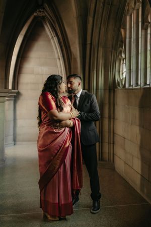 Couple in formal attire sharing tender moment in gothic stone corridor.