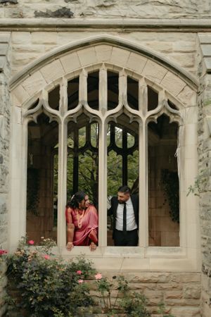 Couple posing through gothic stone window with blooming roses in foreground.