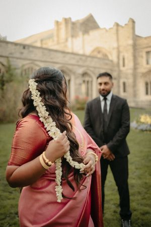 Traditional wedding attire with floral hair garland against historic building backdrop.