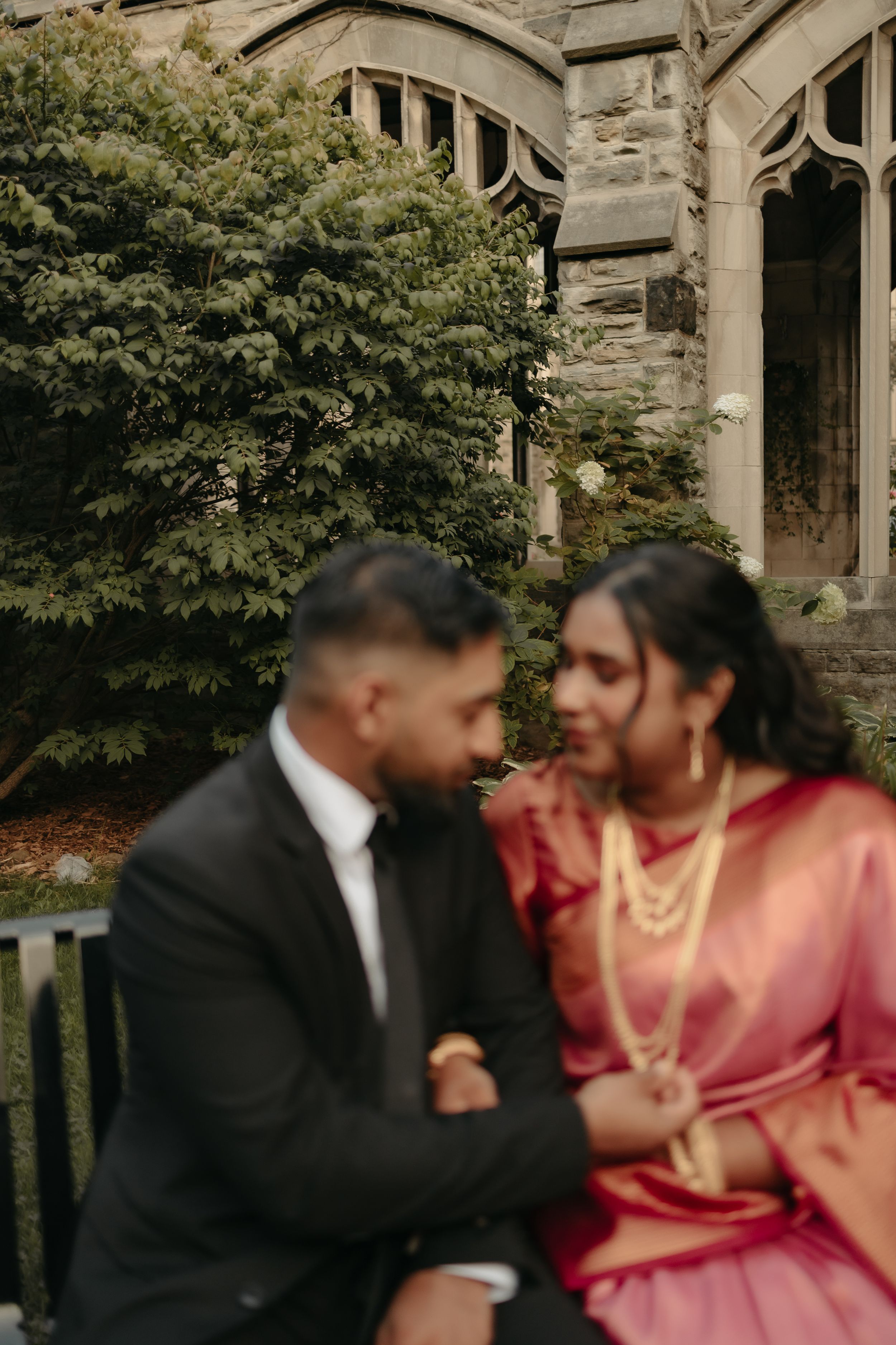 A romantic moment captured on a garden bench against Gothic stone architecture and green foliage.