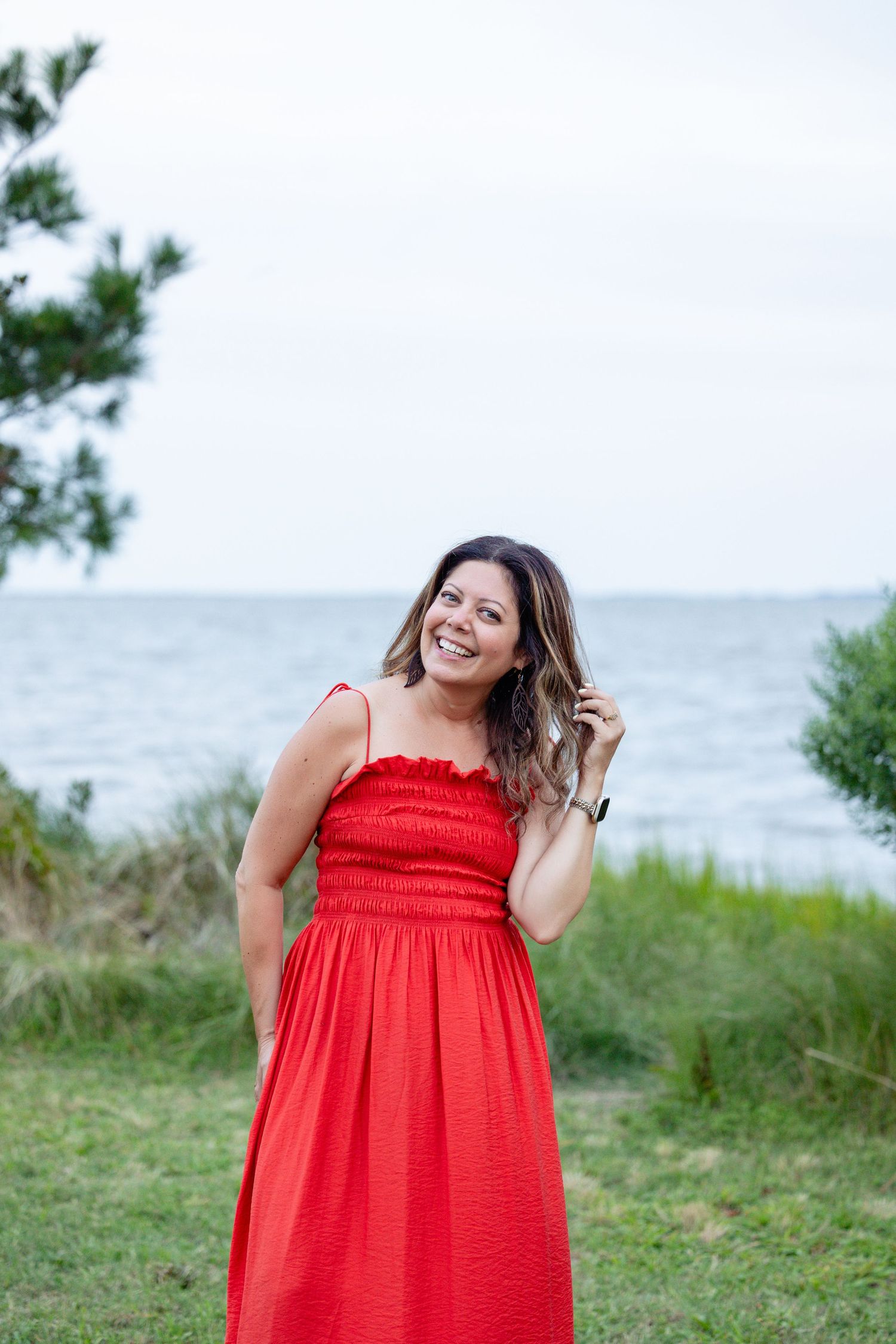 Professional female photographer smiles while holding a DSLR camera outdoors against a blue wall.