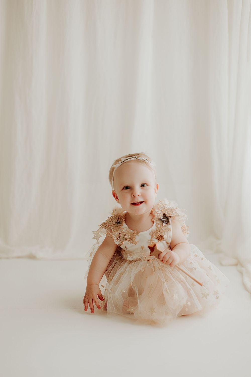 Beautiful baby girl in an elegant gold and cream tulle dress with headband crawling on a white studio floor.