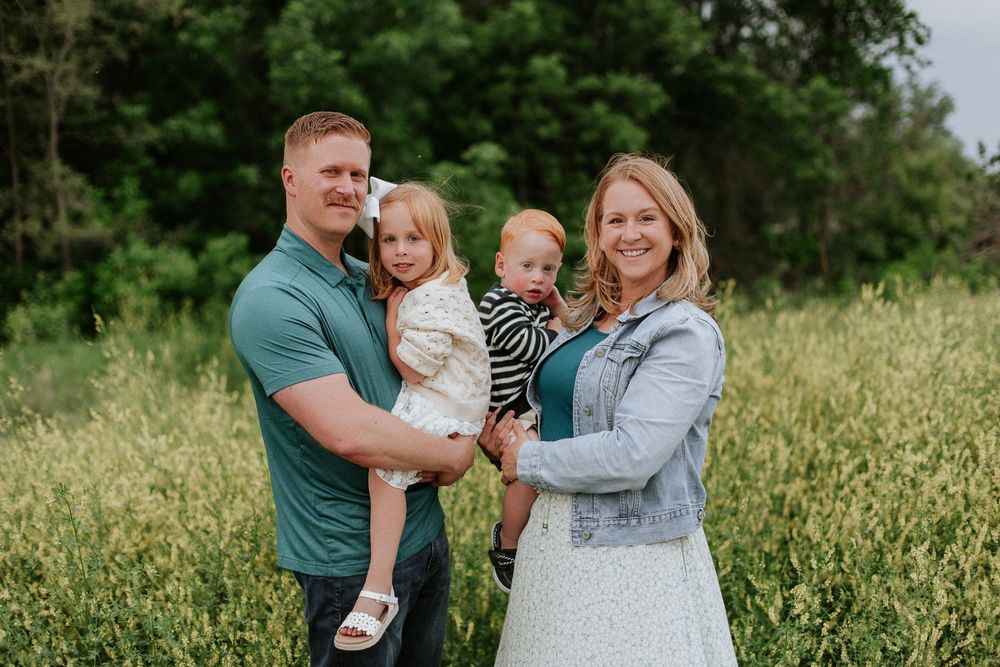 Happy family of four posing together in a lush green field during an outdoor portrait session.