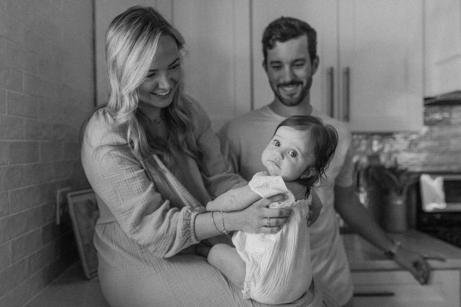 Black and white family photo capturing joyful playtime with baby in the kitchen.