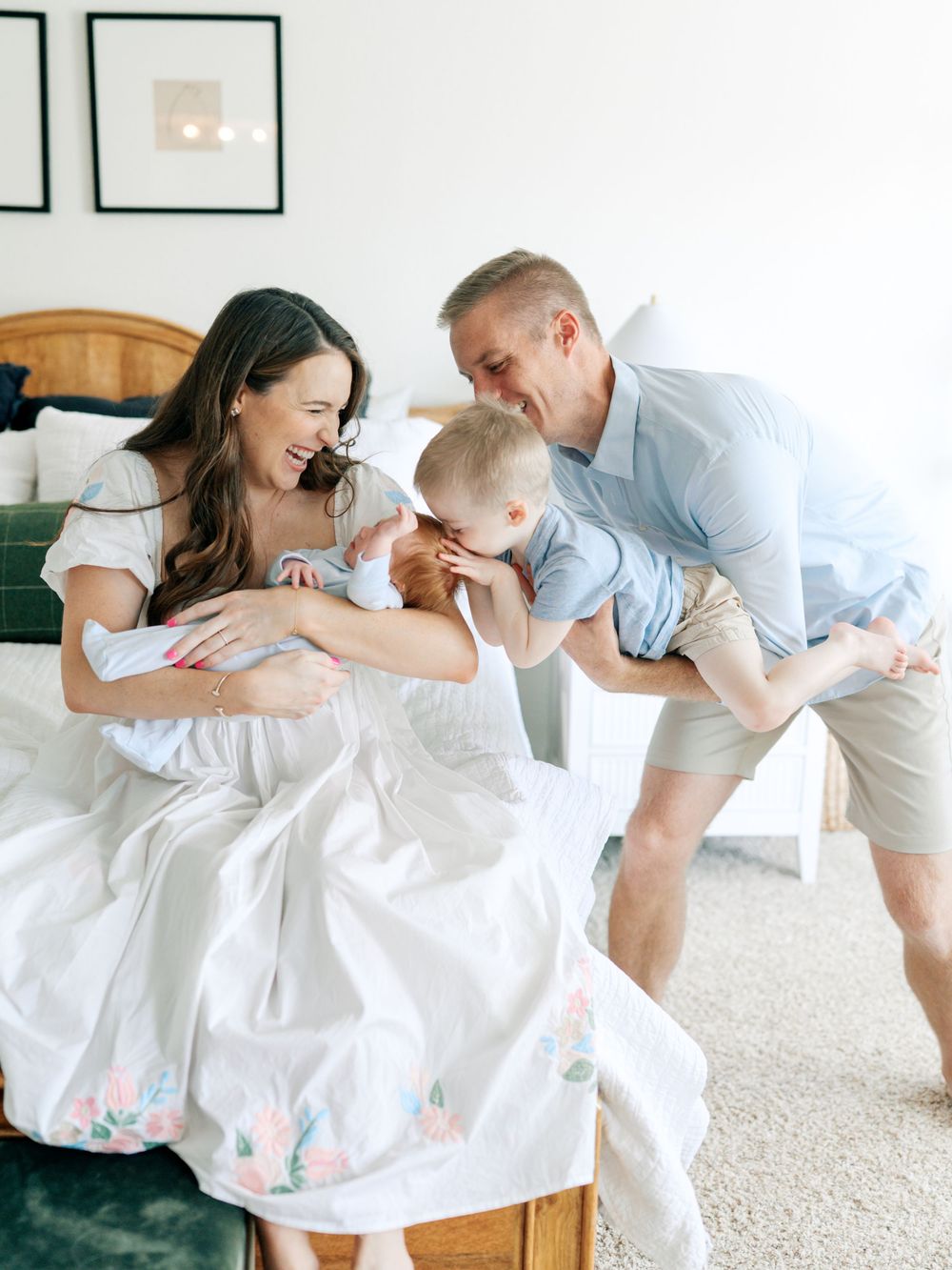 A family wearing white outfits plays and laughs together on a light carpet in a bright, airy room.