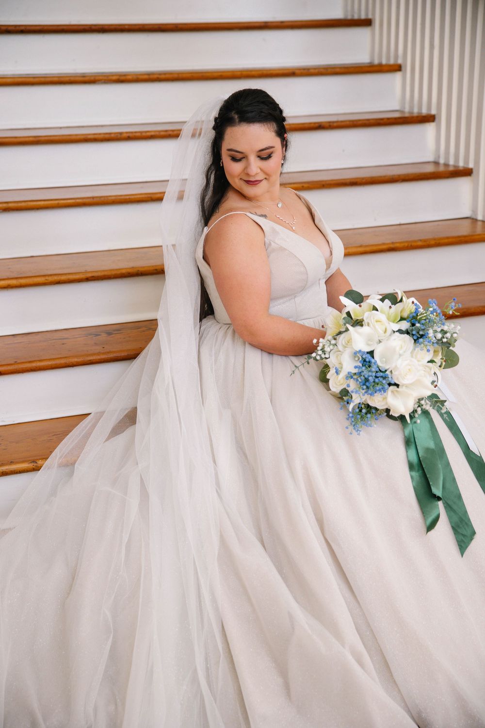 Wedding dress detail shot with blue and white bouquet featuring emerald green ribbons.