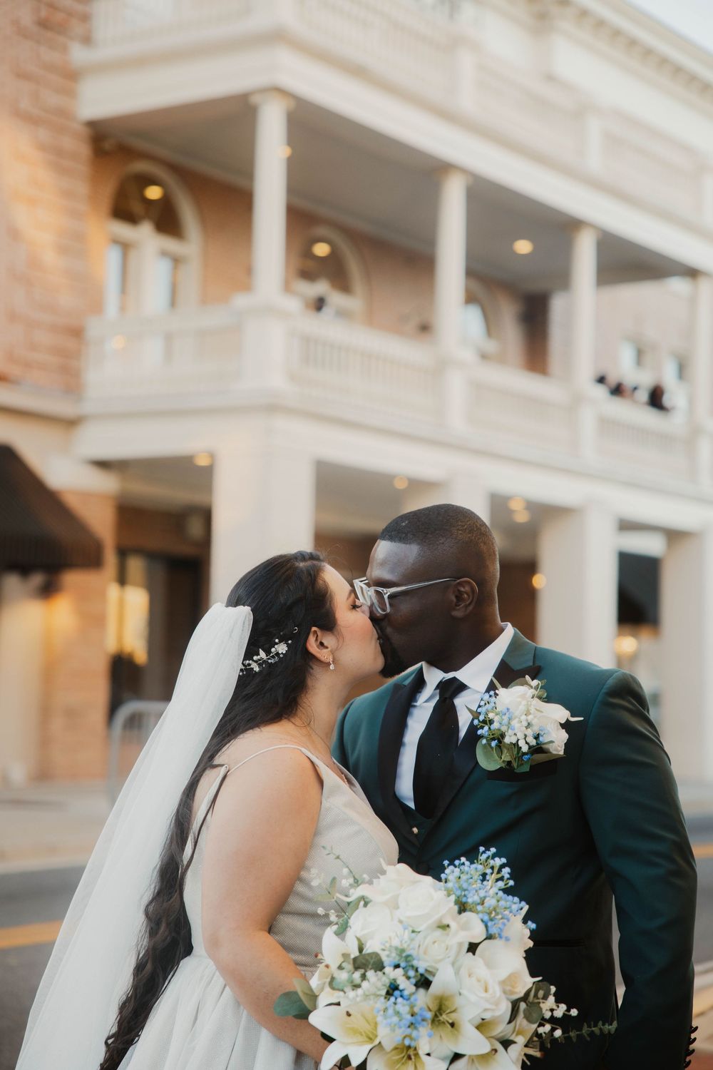 Newlyweds embracing in front of a grand white columned building with floral bouquet details.