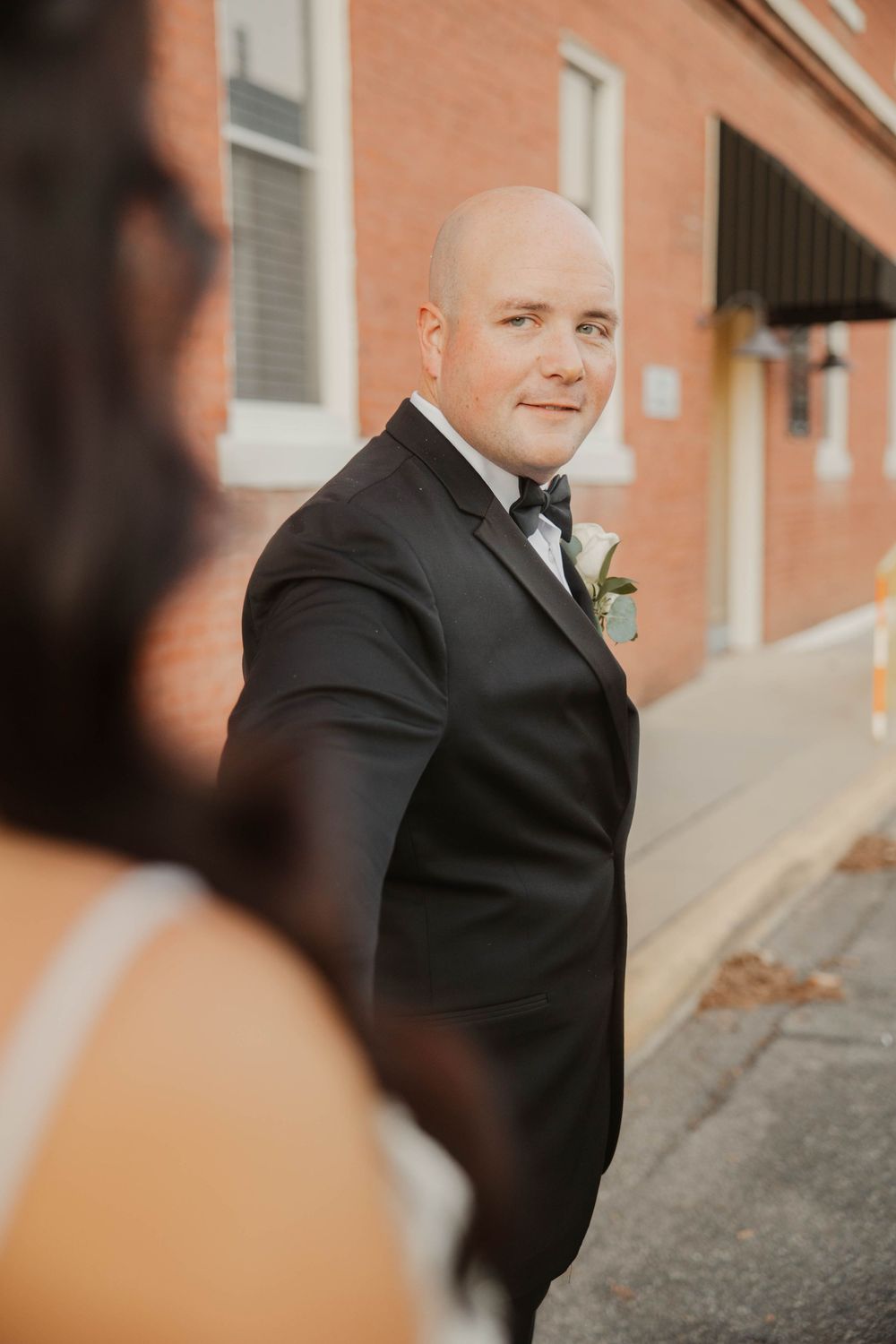 Wedding portrait in warm lighting against a brick wall backdrop.