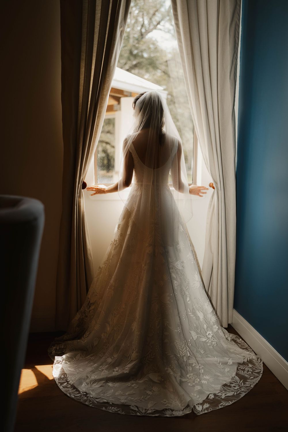Silhouette of a bride in front of a window, showcasing the stunning lace details of her wedding gown.